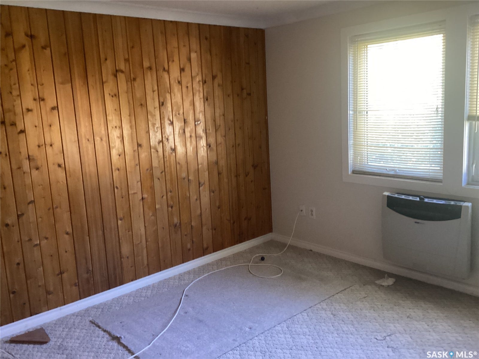 Wood-paneled accent wall, window with blinds, wall-mounted heating unit
