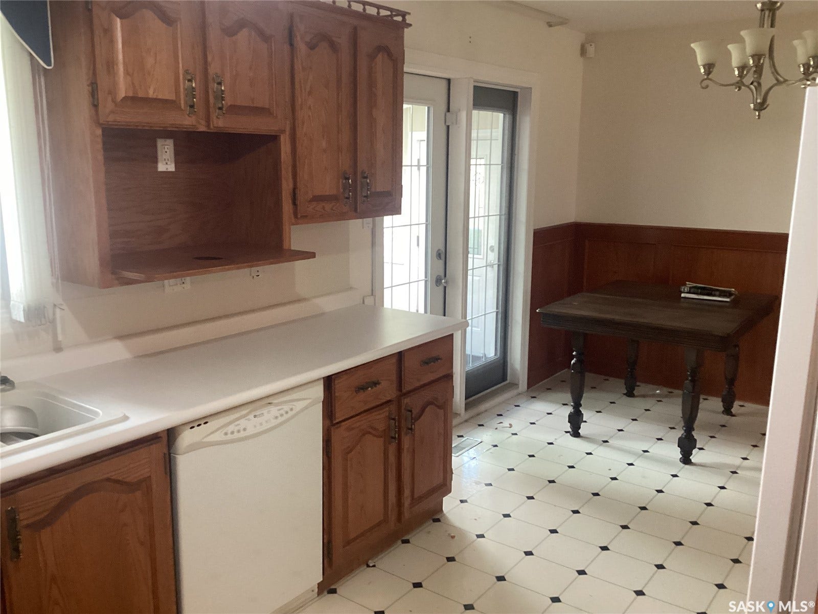 Kitchen featuring wood cabinetry, solid surface countertops, patterned floor tiles, and a built-in dishwasher
