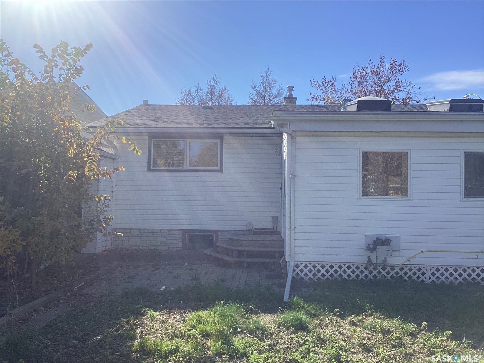 White siding exterior with a shingled roof, featuring multiple windows and a paver patio area