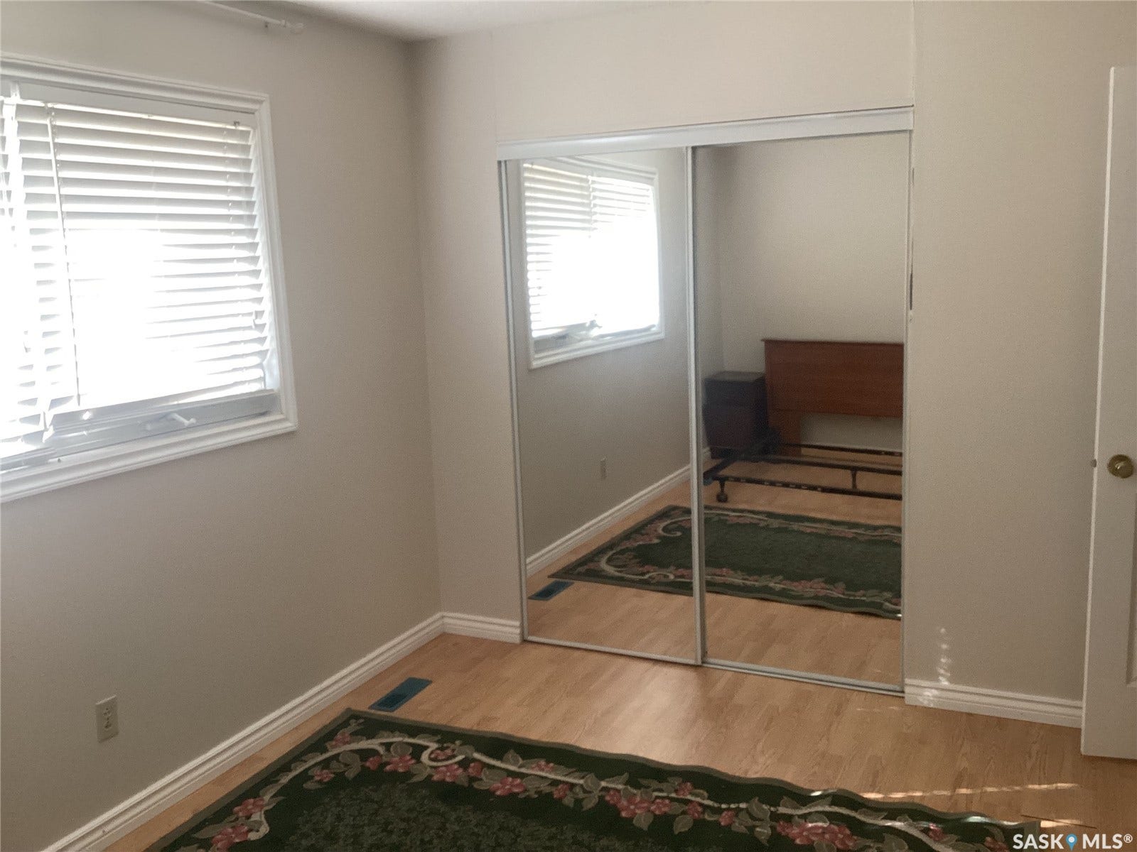 Wood-finish flooring, mirrored sliding closet doors, window with horizontal blinds, neutral wall paint, and white trim