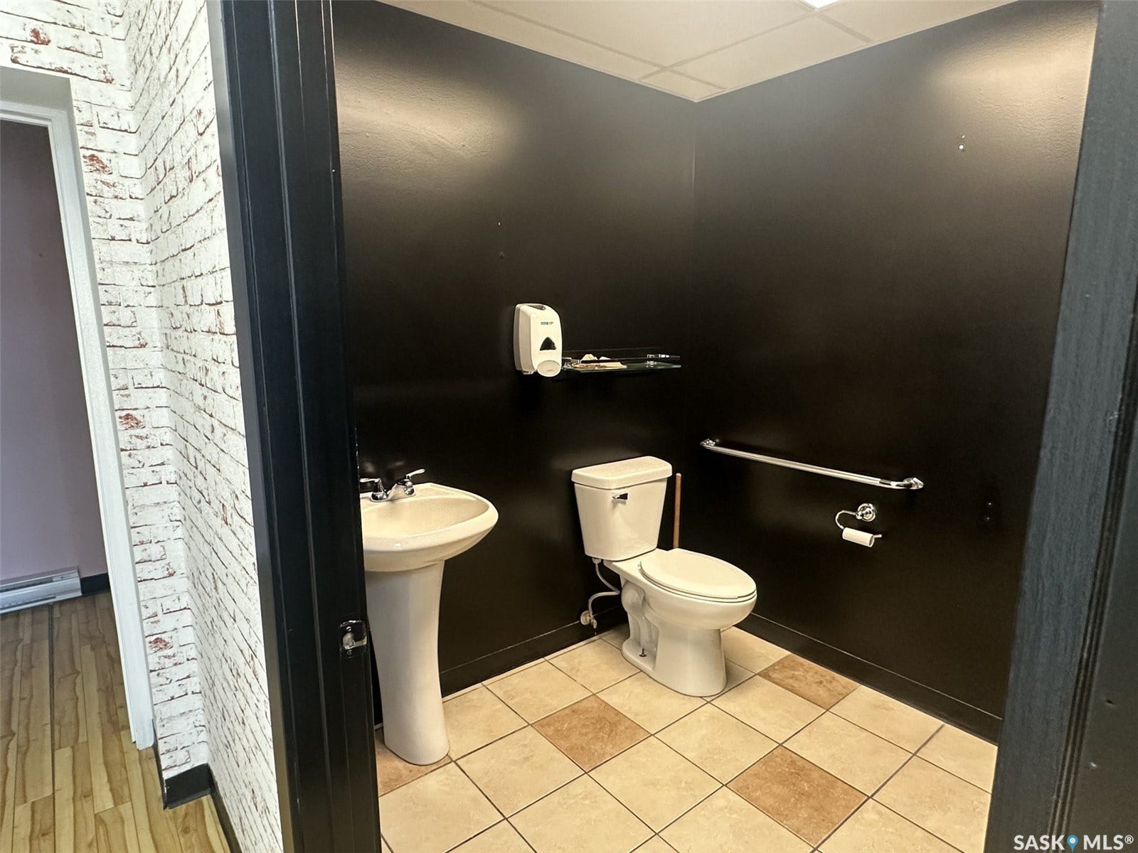 Pedestal sink with chrome fixtures, white toilet, grab bar, and tiled flooring