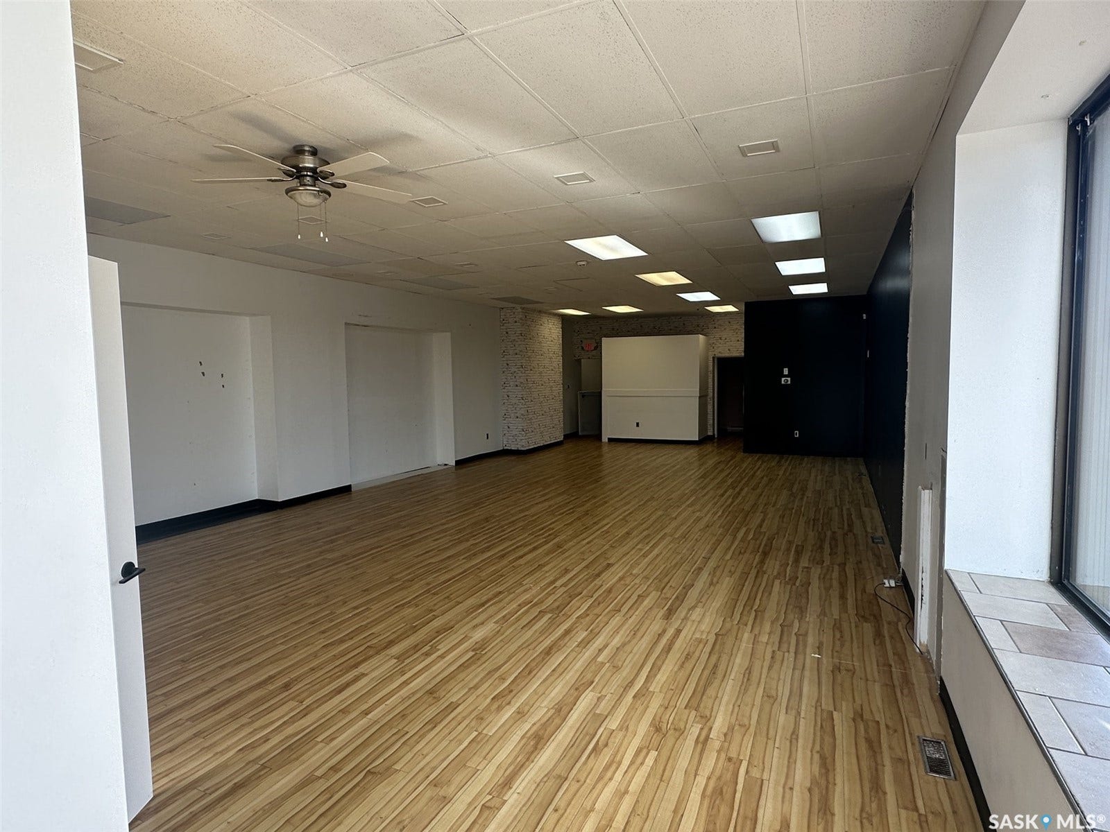 Expansive open area with wood-finish flooring, drop ceiling with recessed lighting, and a ceiling fan