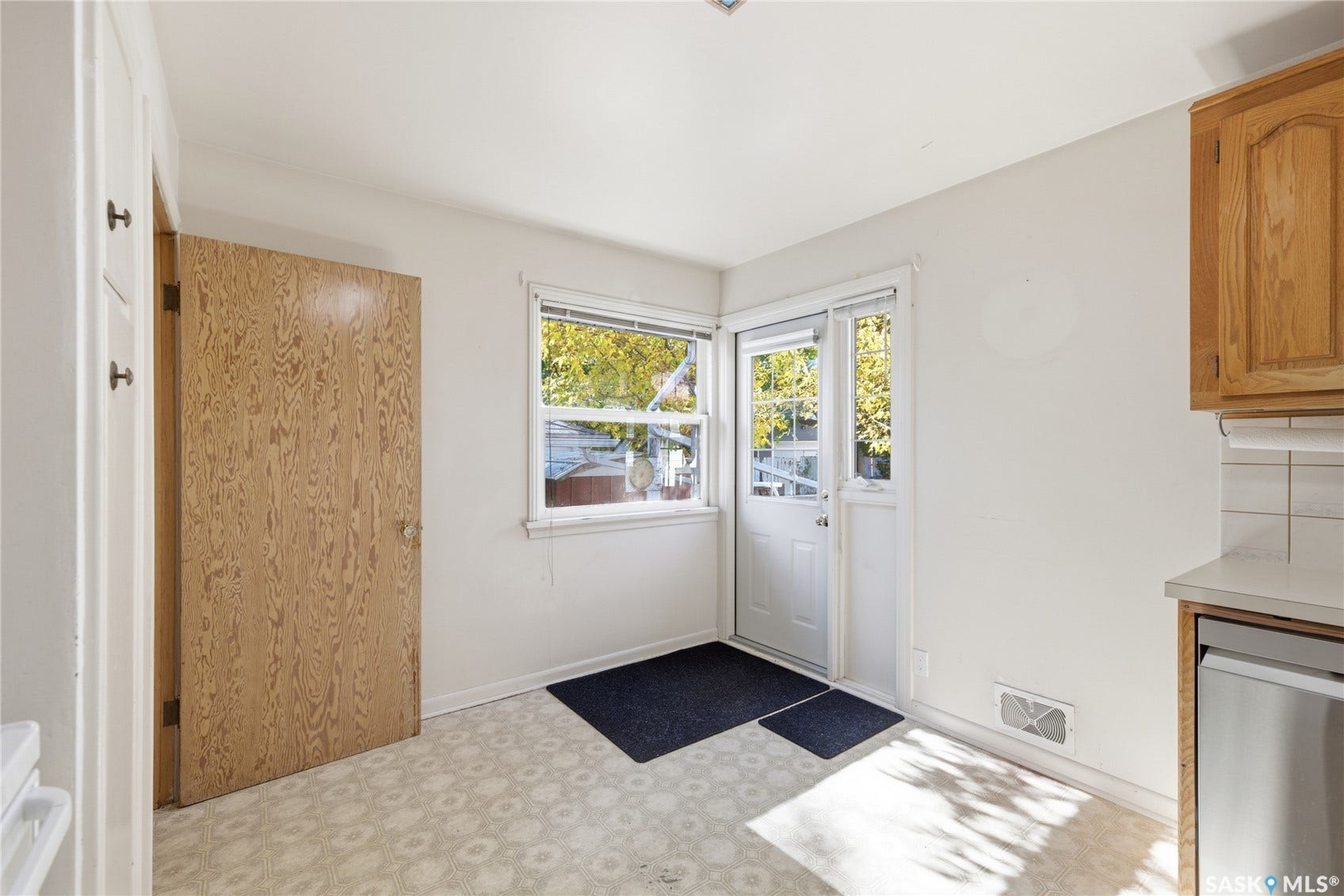 White walls, wood-finish door, light-toned flooring, window with natural light, and a white exterior door