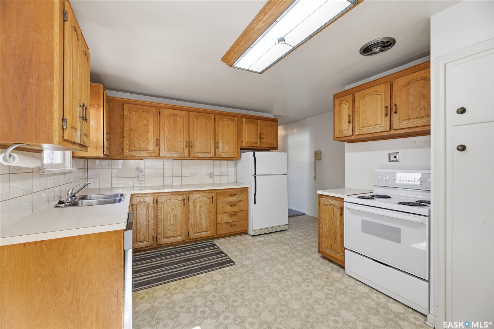 Kitchen featuring extensive wood cabinetry, white countertops, white tile backsplash, and a skylight