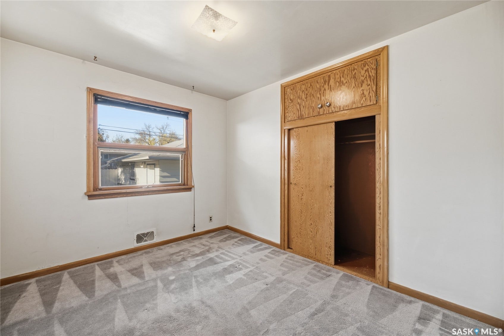 White walls, wood-trimmed window, patterned carpet flooring, wood-finish closet with sliding doors and upper cabinetry, and a ceiling-mounted light fixture