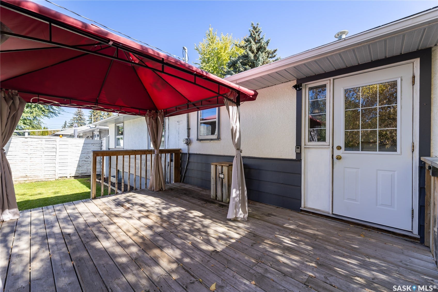 Wood deck with perimeter railing, red fabric gazebo, white exterior siding, dark gray trim, and white exterior door with glass inserts