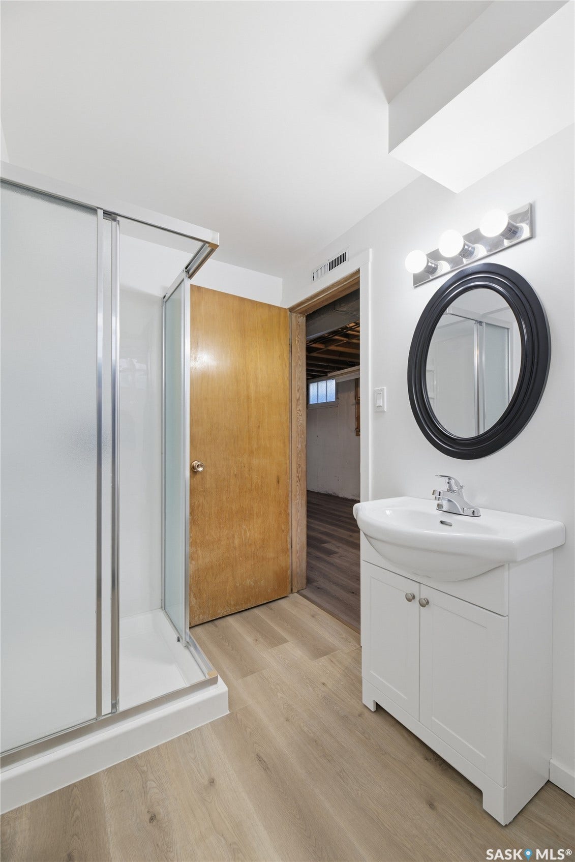 Wood-finish flooring, white vanity with integrated sink, chrome faucet, oval mirror, and chrome vanity light fixture