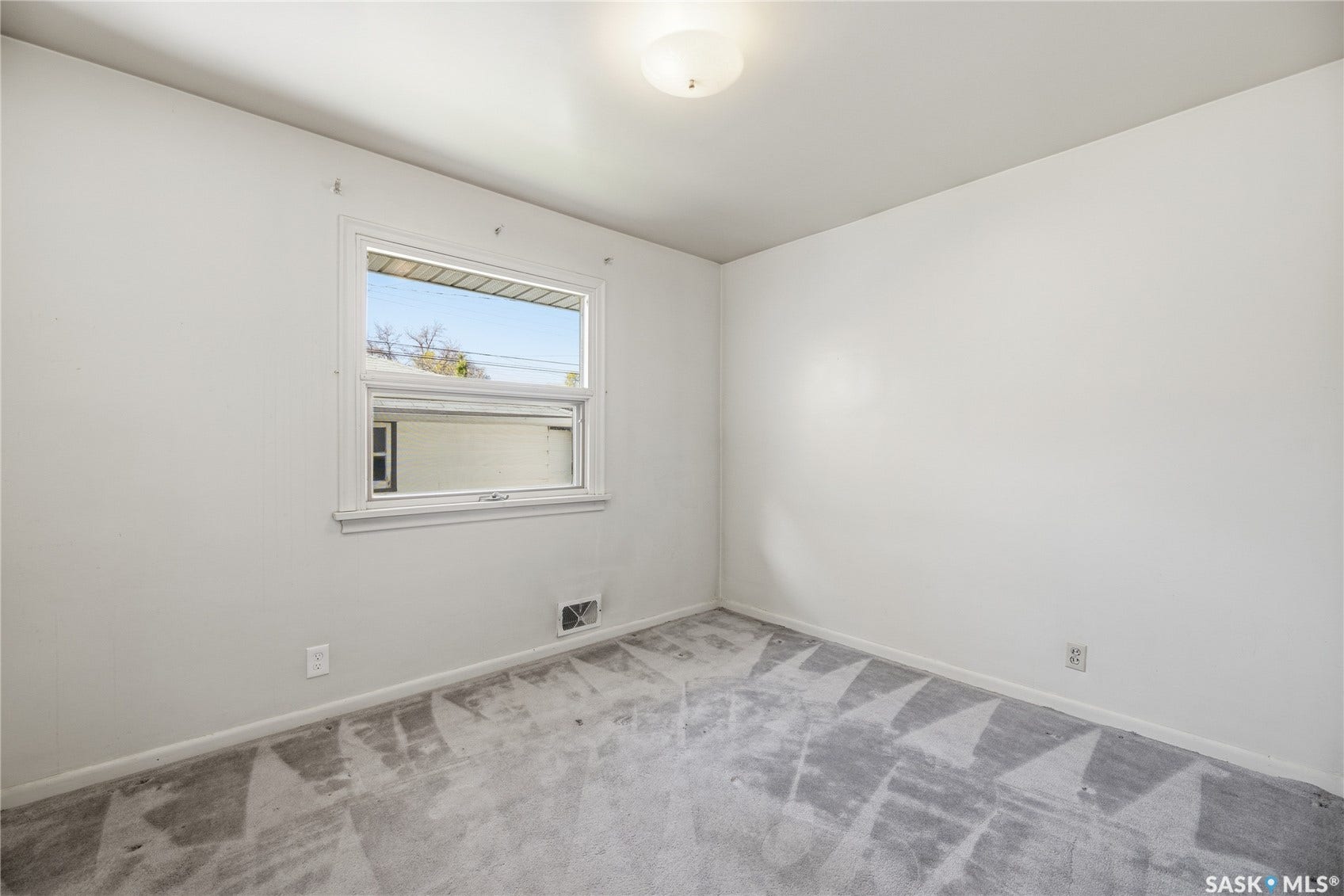 White walls, single window with white trim, ceiling-mounted light fixture, and patterned carpet flooring