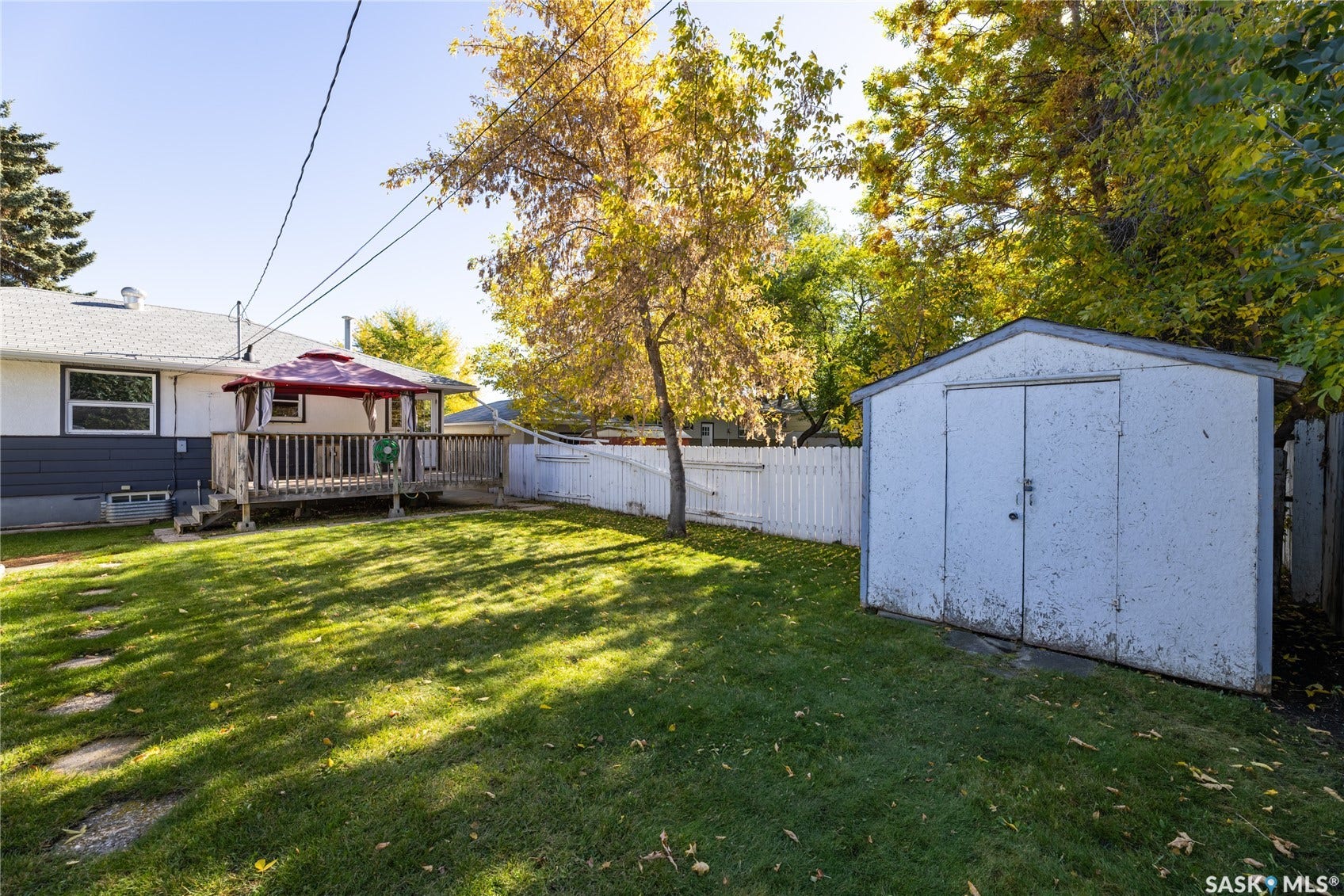 Spacious backyard featuring a wooden deck, a storage shed, and a white picket fence