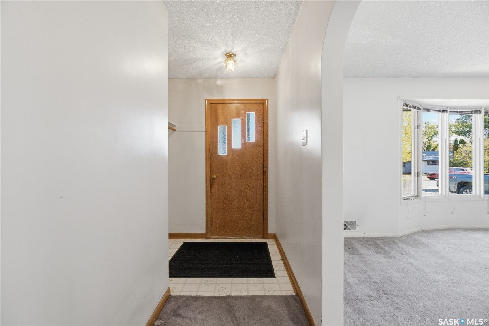 Entryway with a light wood-finish door featuring decorative glass panels, leading to a living area with an arched doorway and a bay window