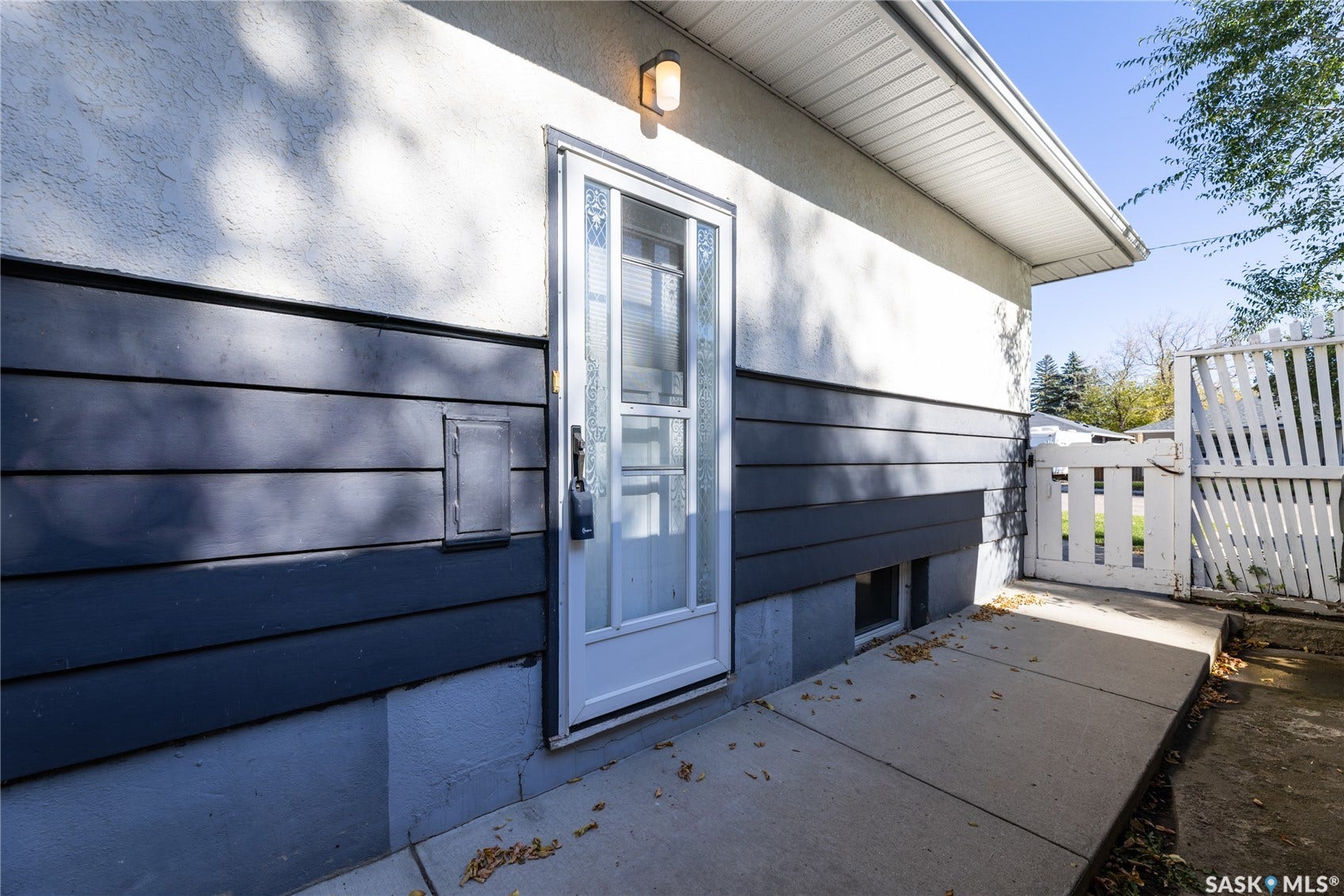 Entry door with storm door, exterior wall with horizontal siding and stucco finish, concrete walkway, and white picket fence