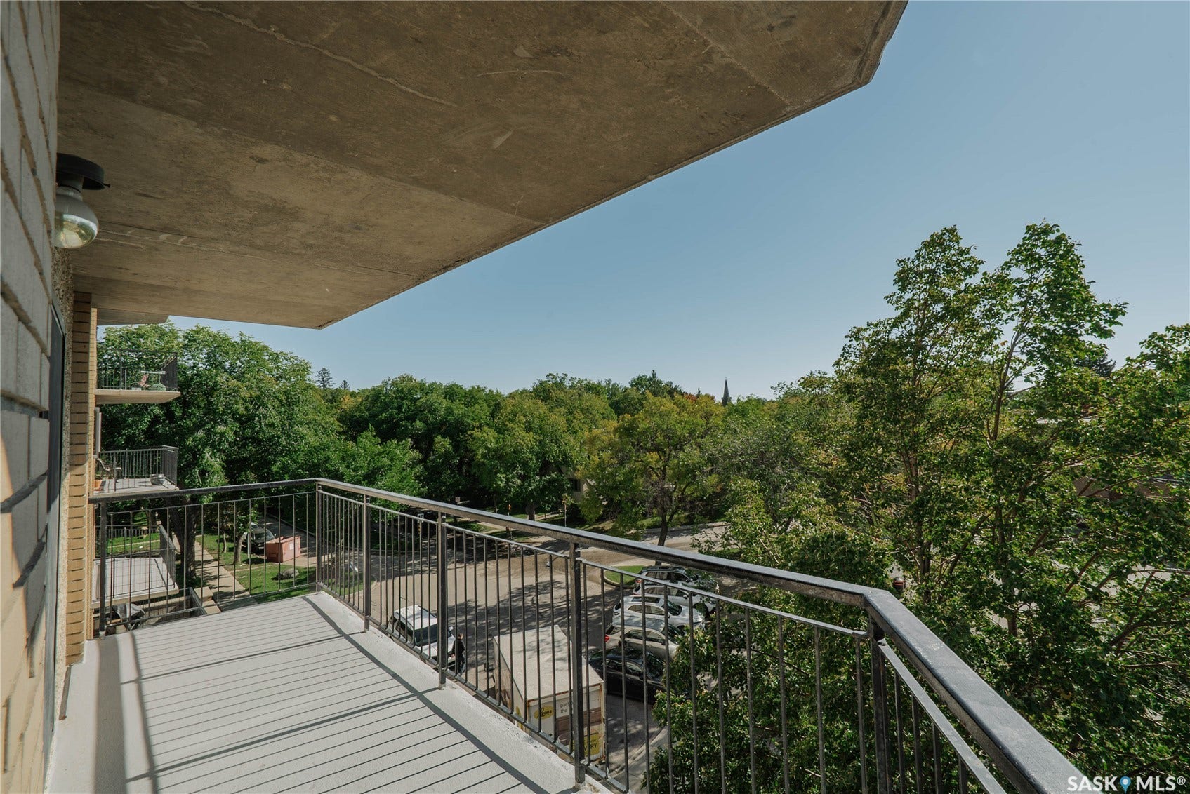 Balcony with metal railing overlooking a tree-lined street