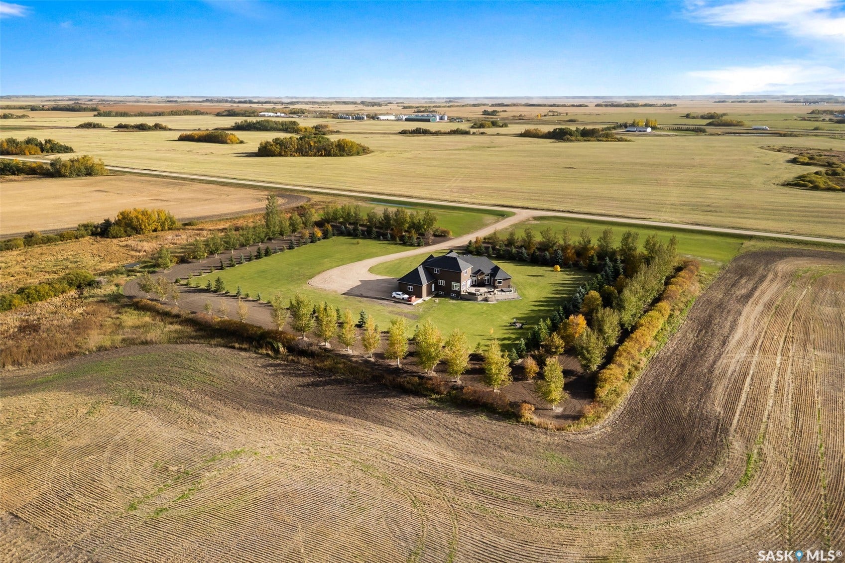 Expansive property with a large residence, circular gravel driveway, manicured lawns, and mature perimeter trees