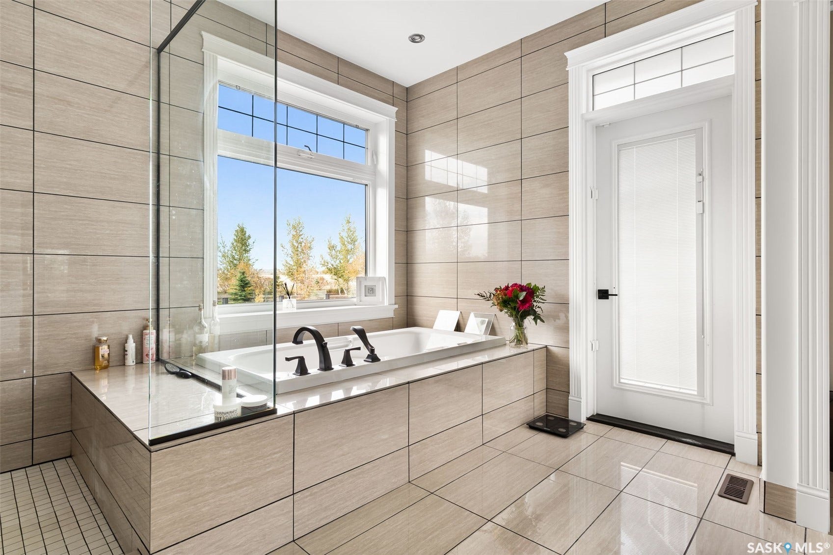 Soaking tub with a multi-pane window, tiled surround, and matte black fixtures