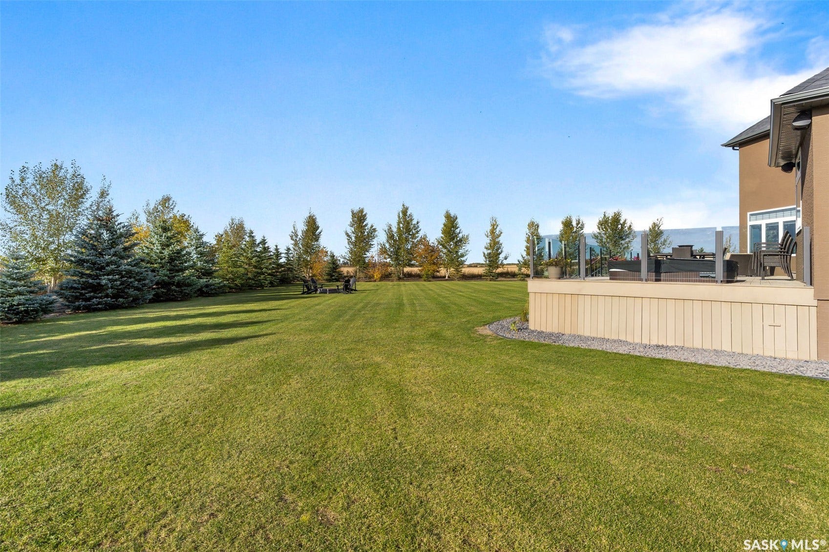 Expansive lawn with mature trees and a raised deck featuring glass railings