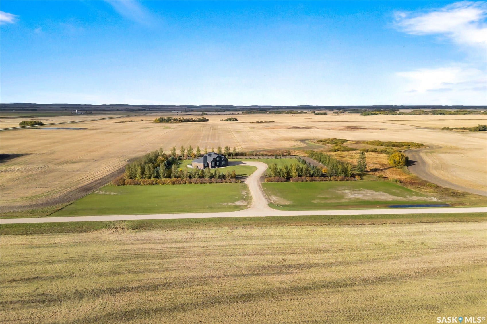 Expansive rural property featuring a modern residence, a gravel drive, and mature trees creating a boundary