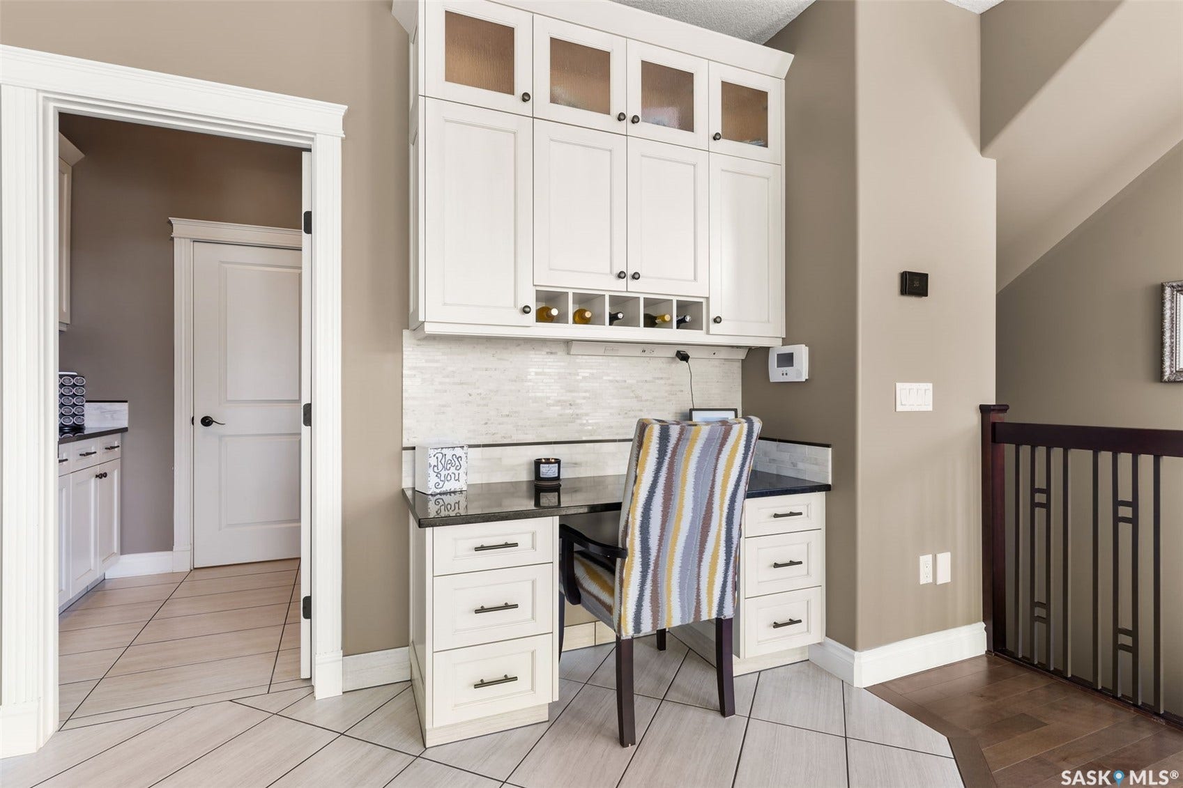 Built-in desk area featuring white cabinetry, dark countertops, and a tiled backsplash
