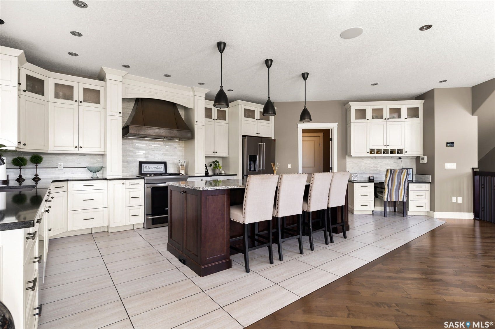 Kitchen featuring white cabinetry, dark countertops, a central island with seating, a built-in desk area, and mixed tile and wood-finish flooring