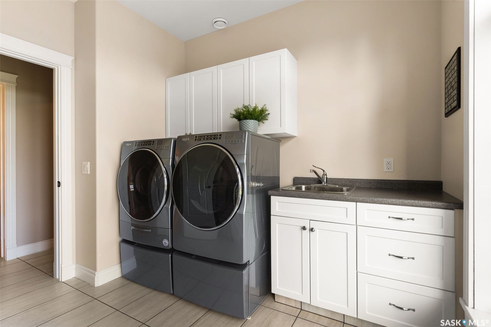 Laundry area featuring light-toned tile flooring, white cabinetry, and a utility sink with a dark countertop