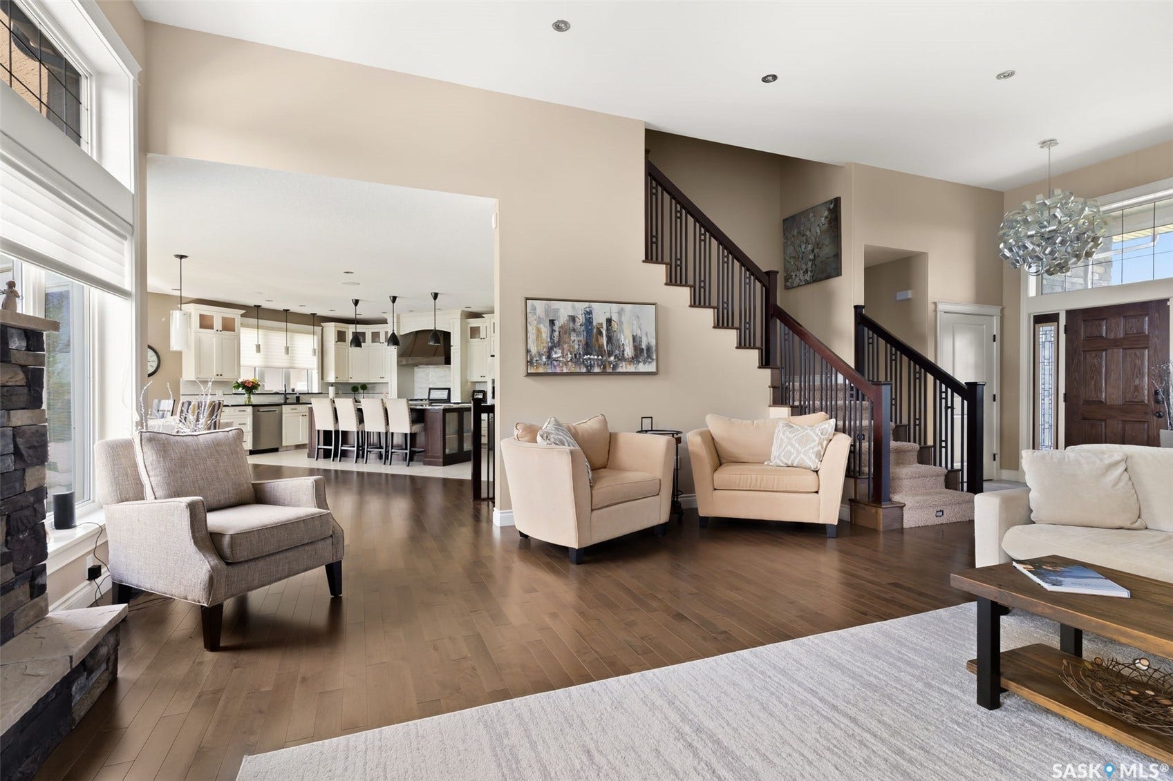 Vaulted ceiling, wood-finish flooring, stone-clad fireplace, integrated kitchen with island seating, and a formal entryway with a wooden door