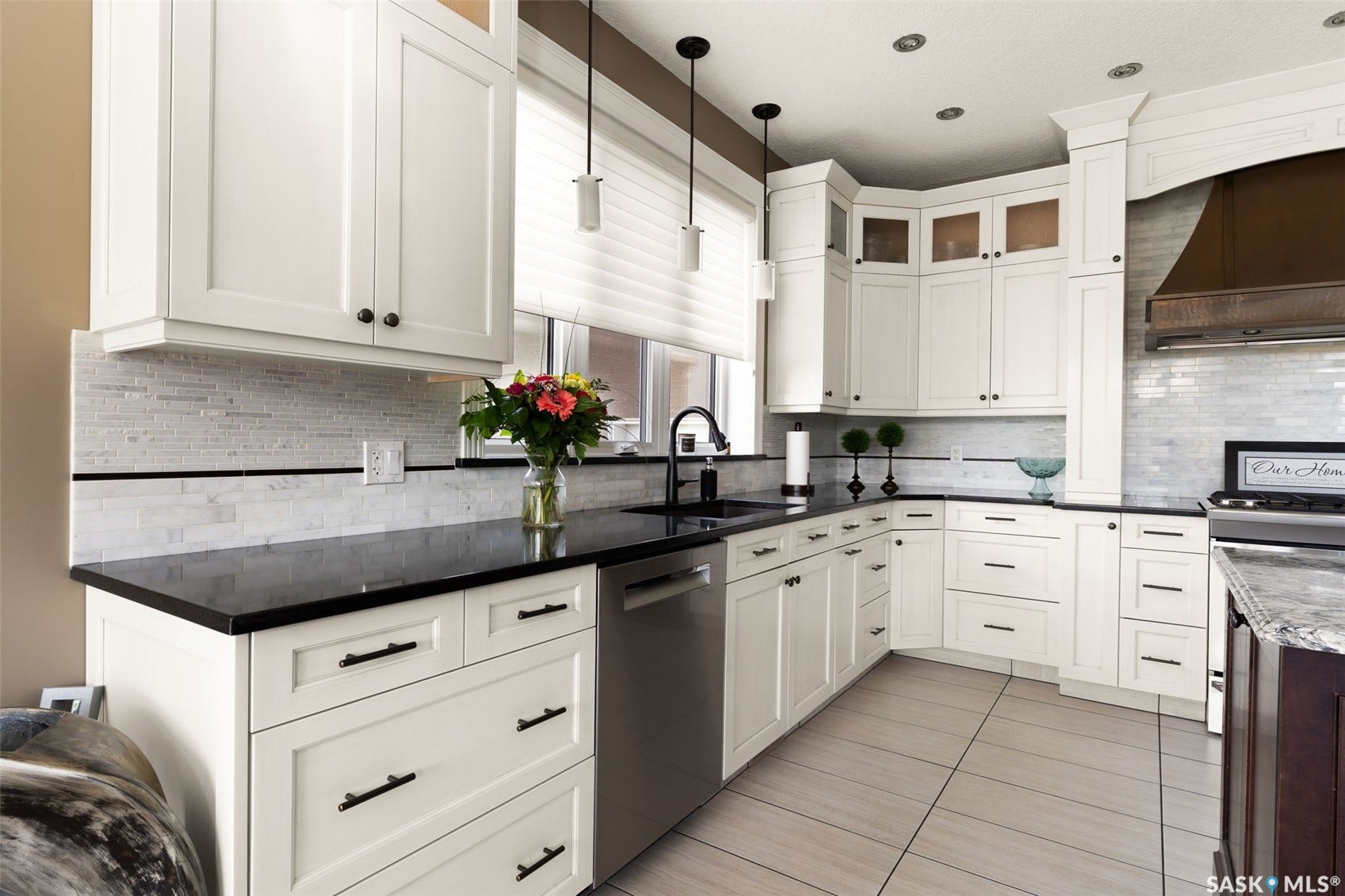 White shaker cabinetry with black hardware, dark countertops, a mosaic tile backsplash, stainless steel appliances, and light-toned tile flooring