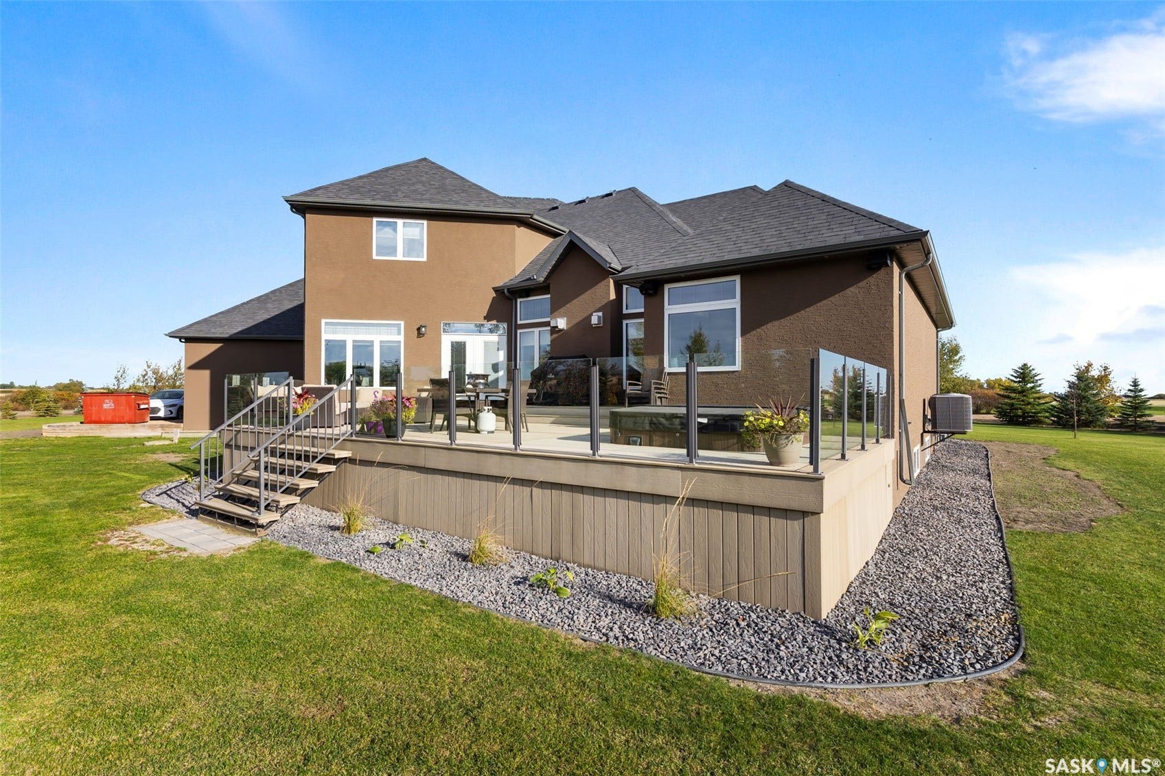 Expansive multi-level deck with glass railing, stucco exterior, multiple windows, dark shingle roof, and exterior stairs with metal railing
