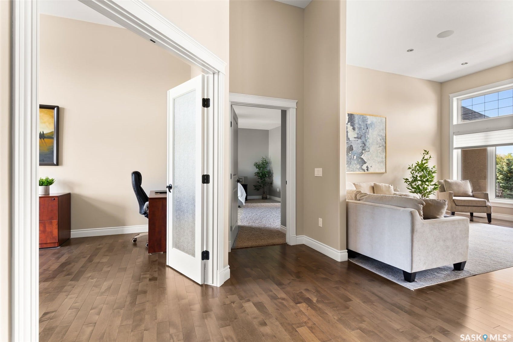 Wood-finish flooring throughout, featuring a private office with a frosted glass door, and a living area with high ceilings and expansive windows