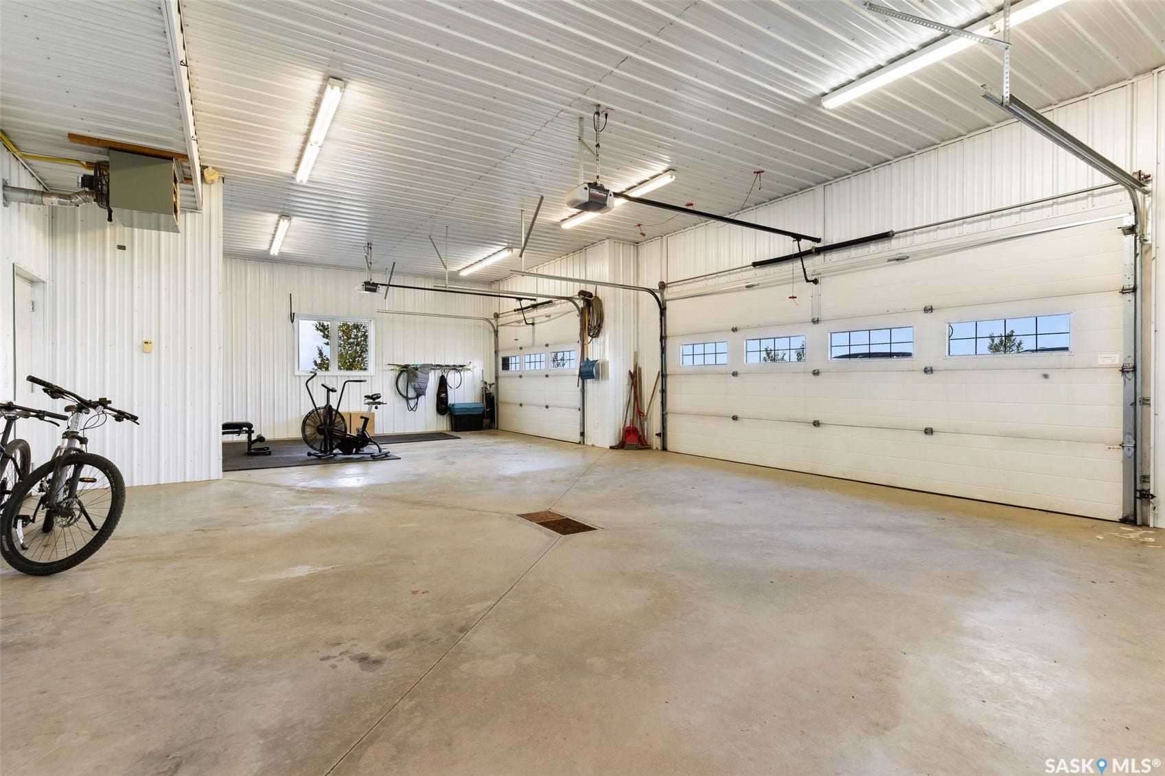 Spacious garage featuring a concrete floor, two overhead doors with window panels, multiple fluorescent lighting fixtures, and corrugated metal walls