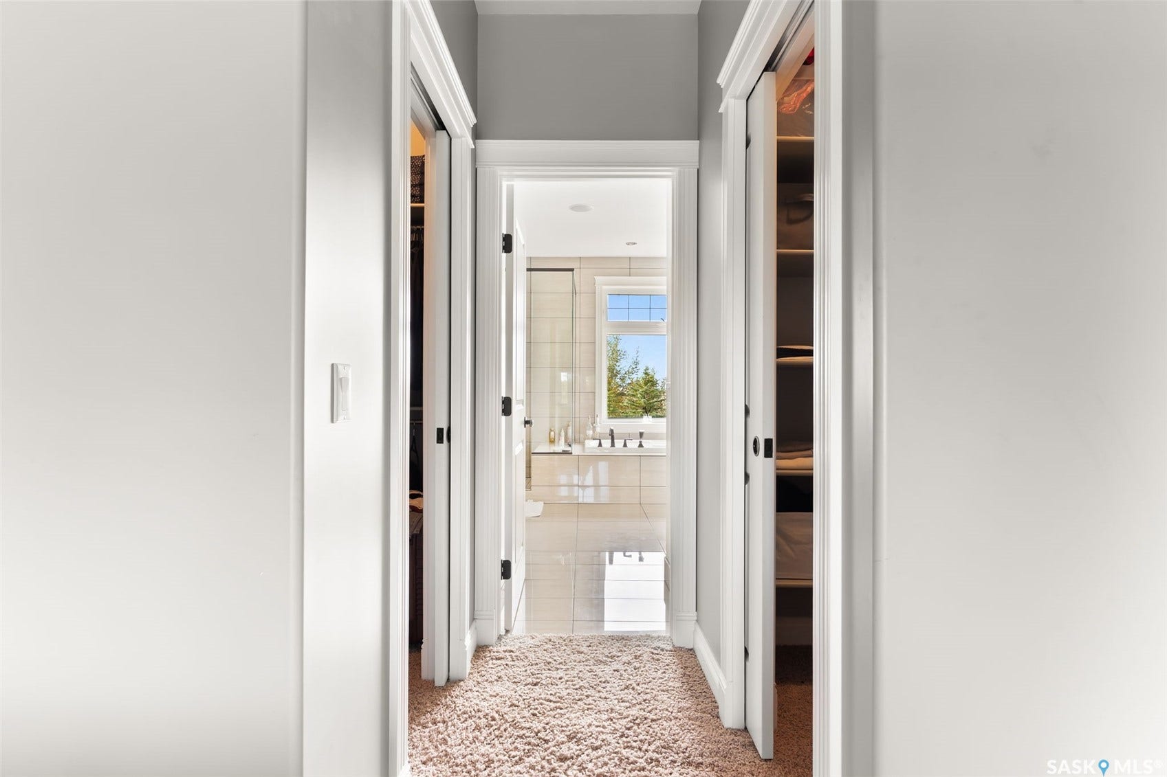 Hallway featuring plush carpeting and white trim, leading to a bathroom with a window and tiled walls