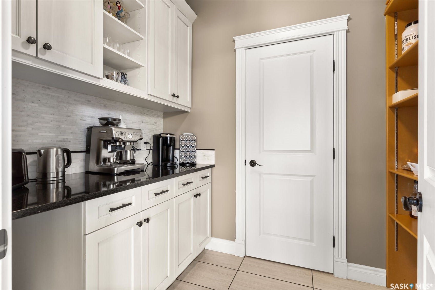 White cabinetry with dark hardware, dark countertops, tiled backsplash, built-in open shelving, and tiled flooring