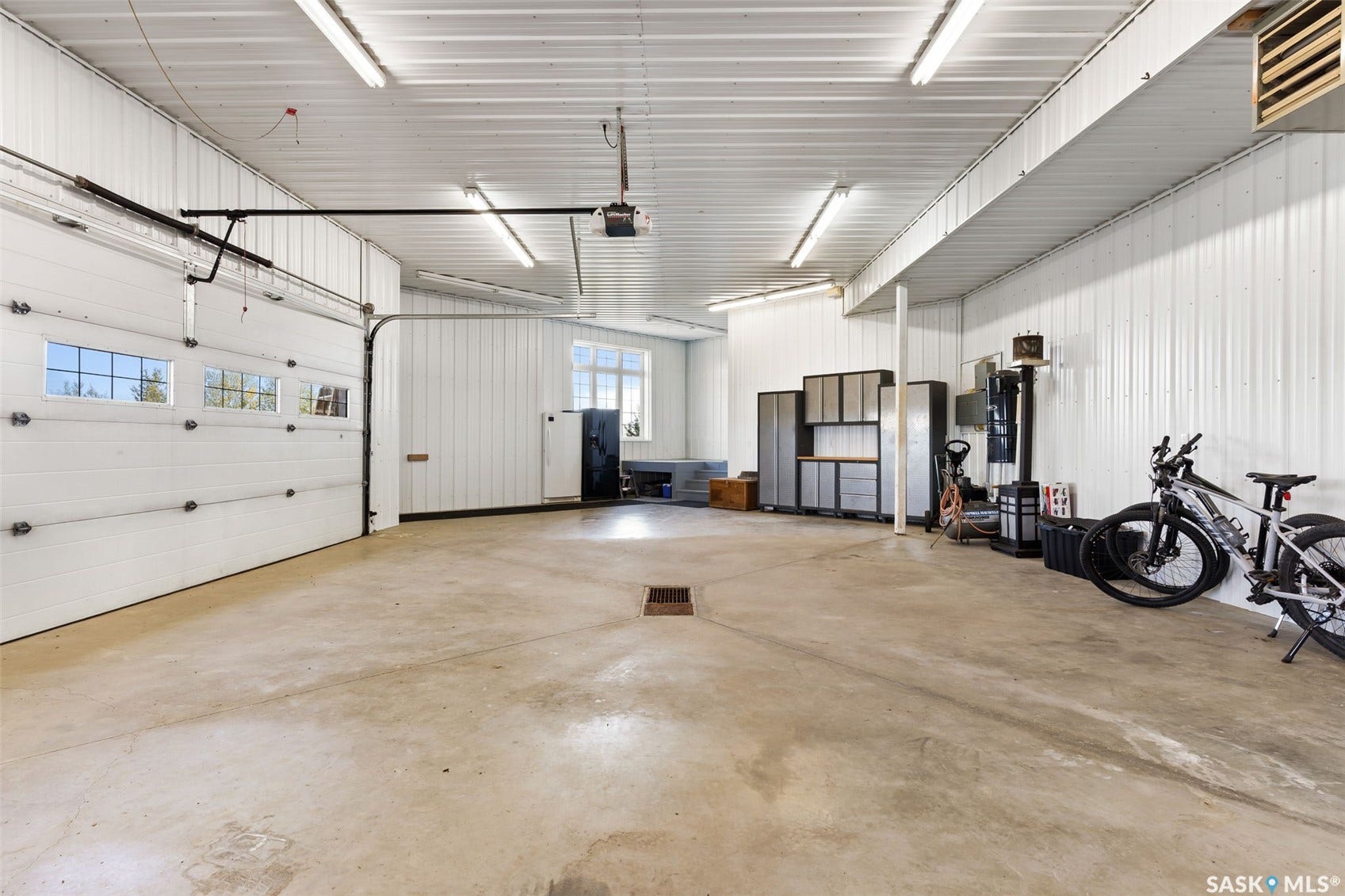 Spacious garage with high ceilings, concrete flooring, overhead lighting, and white paneled walls