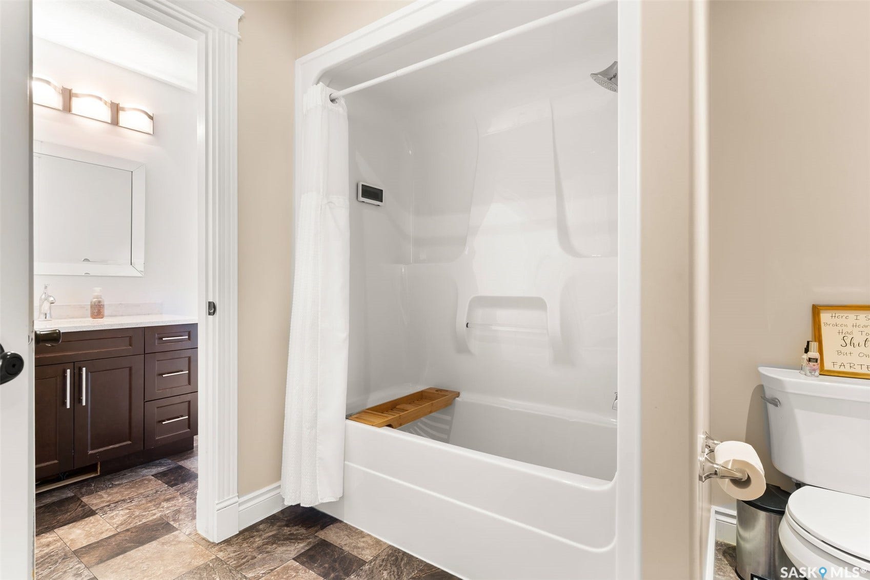 White bathtub with an integrated shower, adjacent to a vanity with a white countertop and dark wood-finish cabinetry