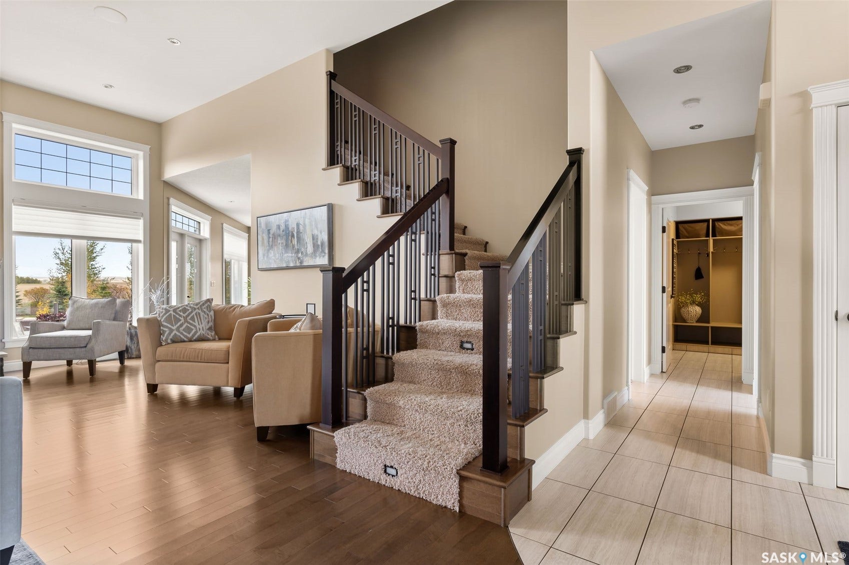 Hardwood flooring, carpeted staircase with integrated lighting, dark wood newel posts and balusters, tall windows with transom details, and a tiled hallway