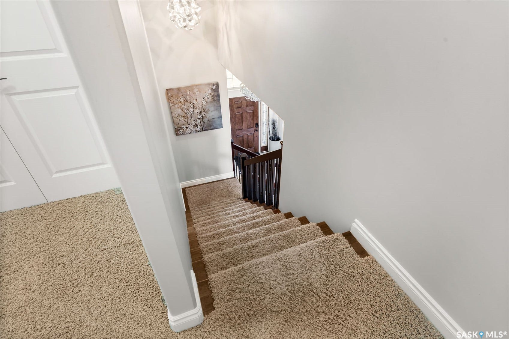Staircase with carpeted treads and wood risers, featuring a dark wood handrail and balusters, with a decorative light fixture above