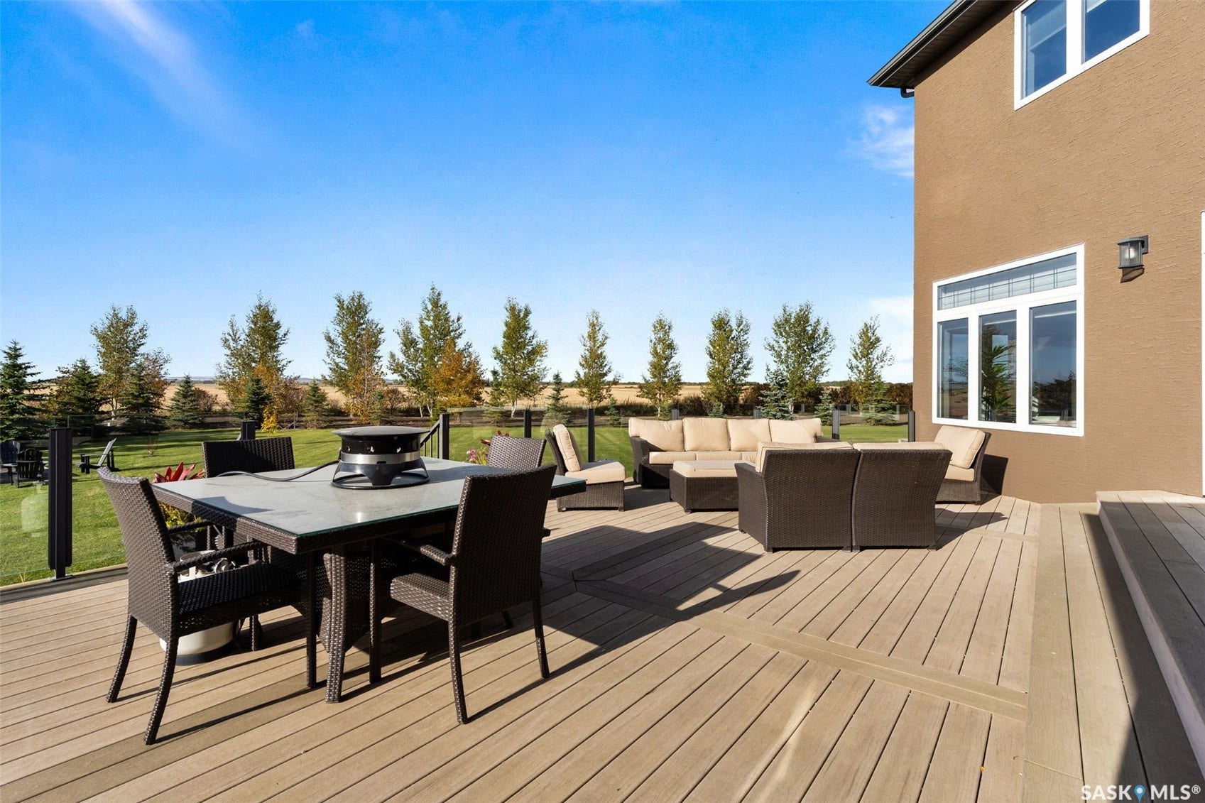 Expansive outdoor deck with composite decking, glass panel railing, stucco exterior, and multiple windows