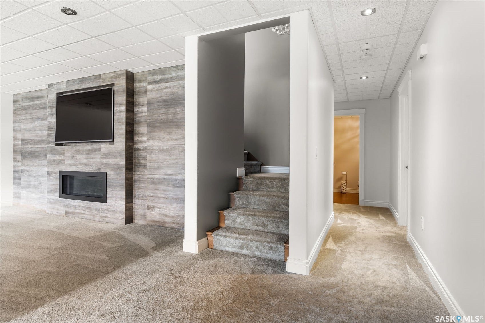 Wall-mounted television with an integrated linear fireplace, textured tile accent wall, carpeted flooring, and recessed lighting