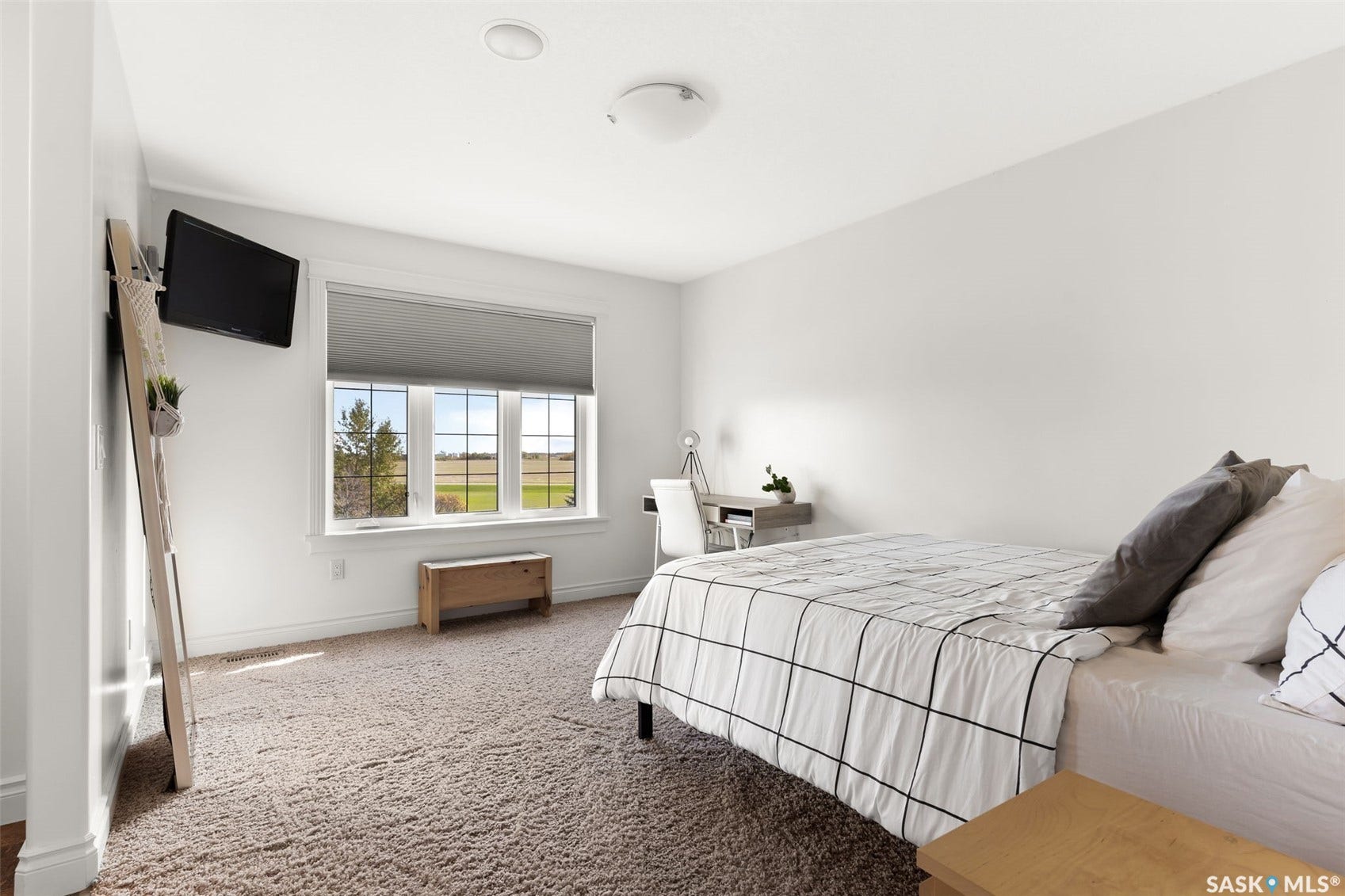 Wall-mounted television fixture, large window with blinds, recessed ceiling lighting, textured carpeting, and white wall finishes