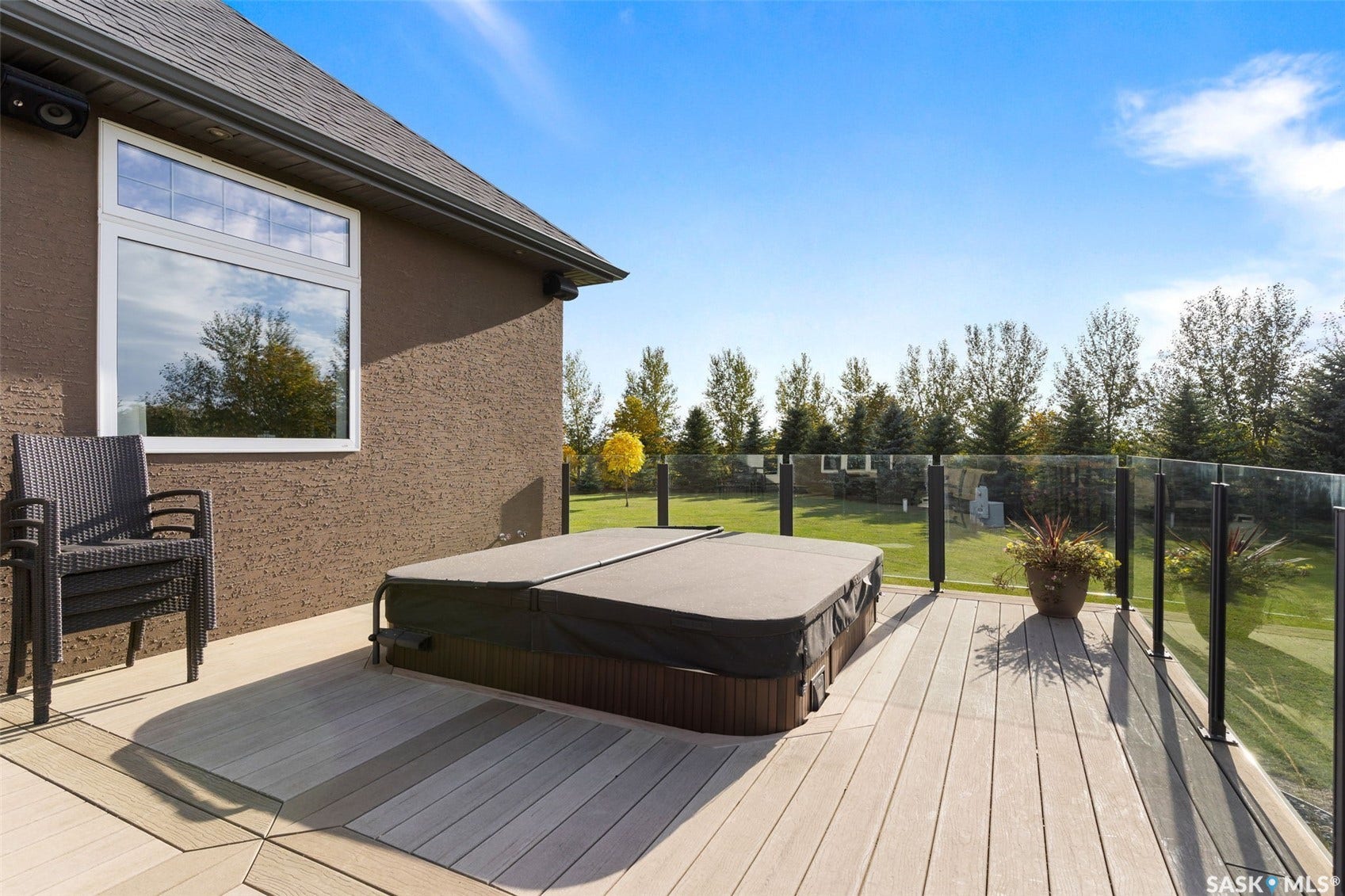 Outdoor deck with a covered hot tub, glass railing, and textured exterior wall