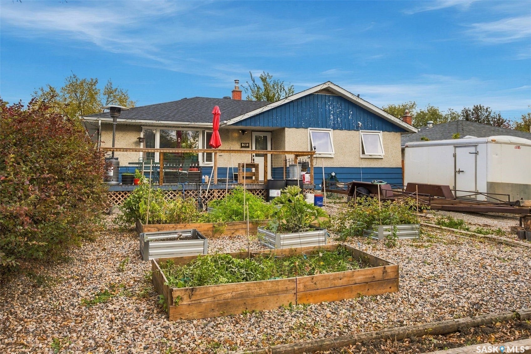 Expansive backyard featuring multiple raised garden beds, a gravel-covered surface, and a wooden deck