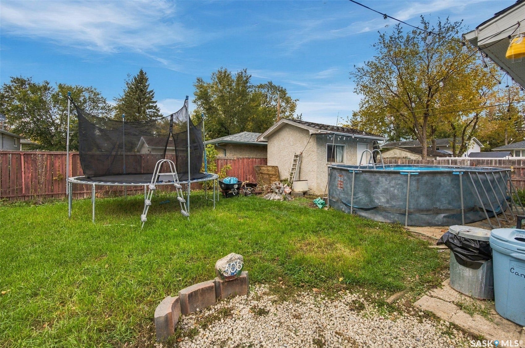 Spacious backyard featuring a mature landscaped lawn, established trees, and multiple recreational amenities including a trampoline and above-ground pool