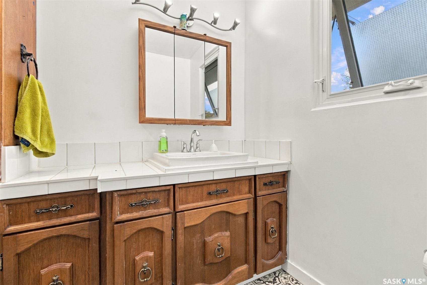 Wood-finish vanity with ample storage, a white tile countertop, and a surface-mounted sink