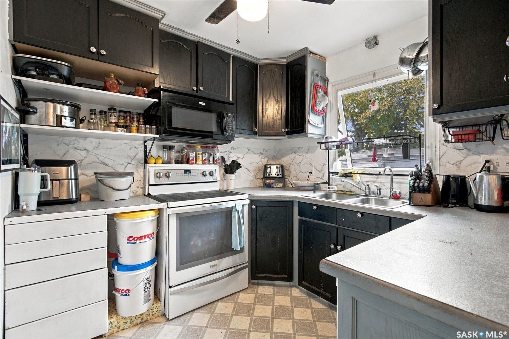 Black cabinetry with chrome hardware, white tile backsplash, stainless steel sink, and a built-in microwave
