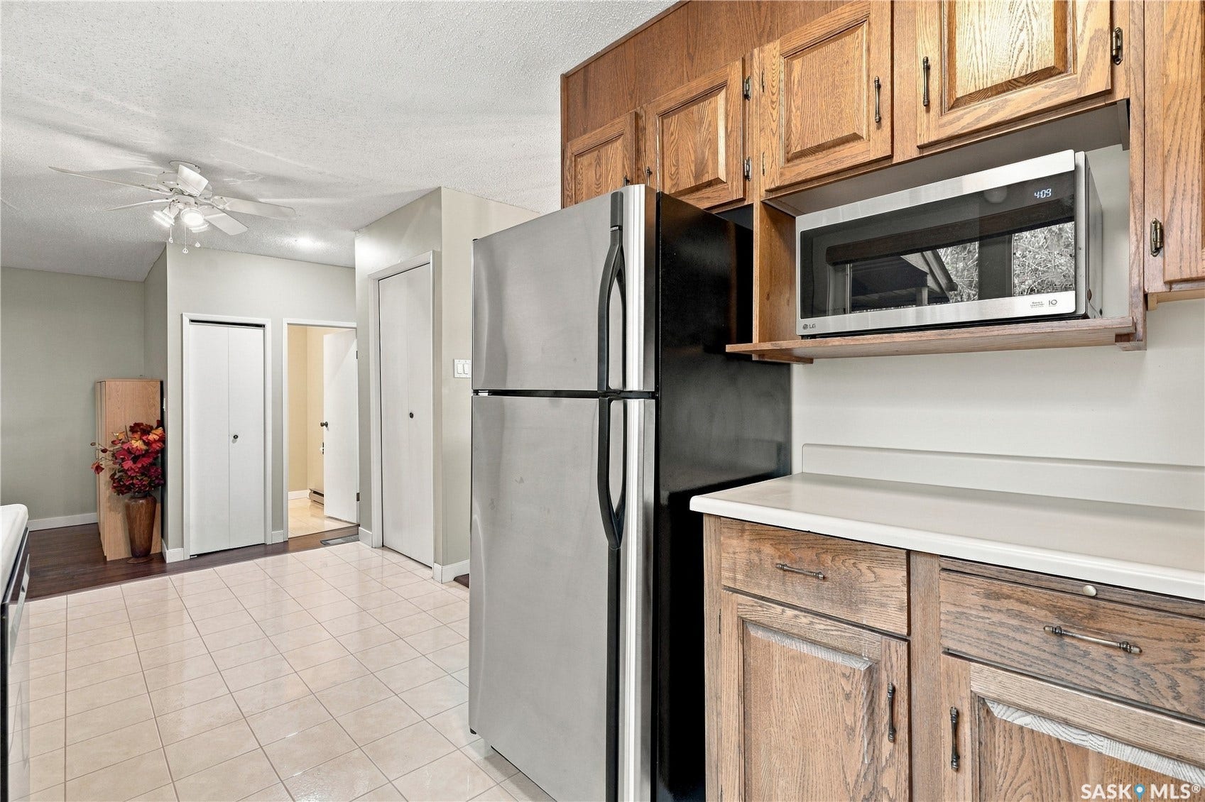 Stainless steel refrigerator, integrated microwave, wood cabinetry with dark hardware, light-toned countertops, and tiled flooring
