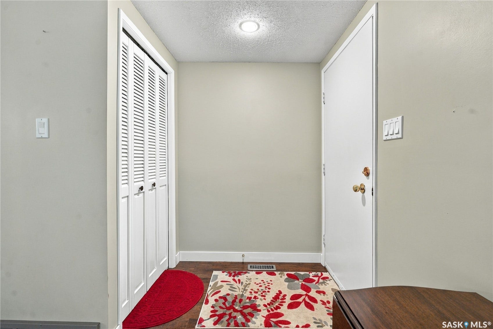 Entryway with wood-finish flooring, a white solid-core door, and a built-in closet with louvered bifold doors