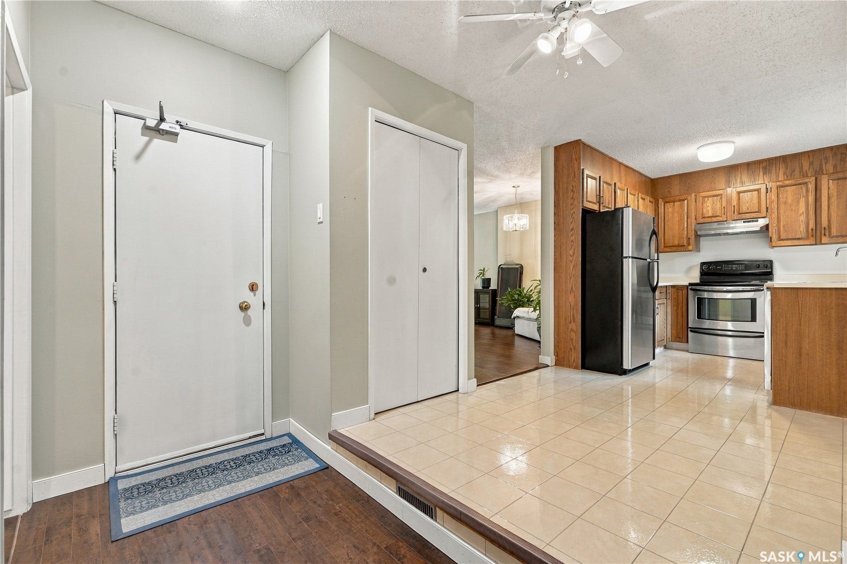 Foyer with wood-finish flooring transitioning to a tiled kitchen featuring wood cabinetry and stainless steel appliances