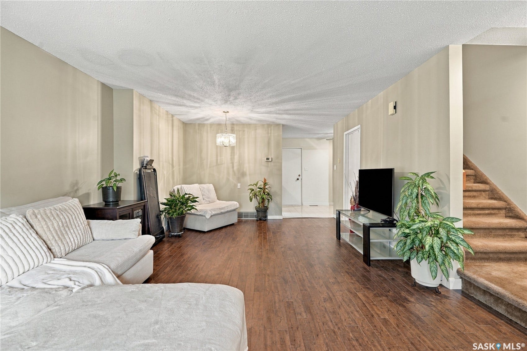 Expansive living area featuring wood-finish flooring, neutral wall tones, a contemporary chandelier, and a carpeted staircase