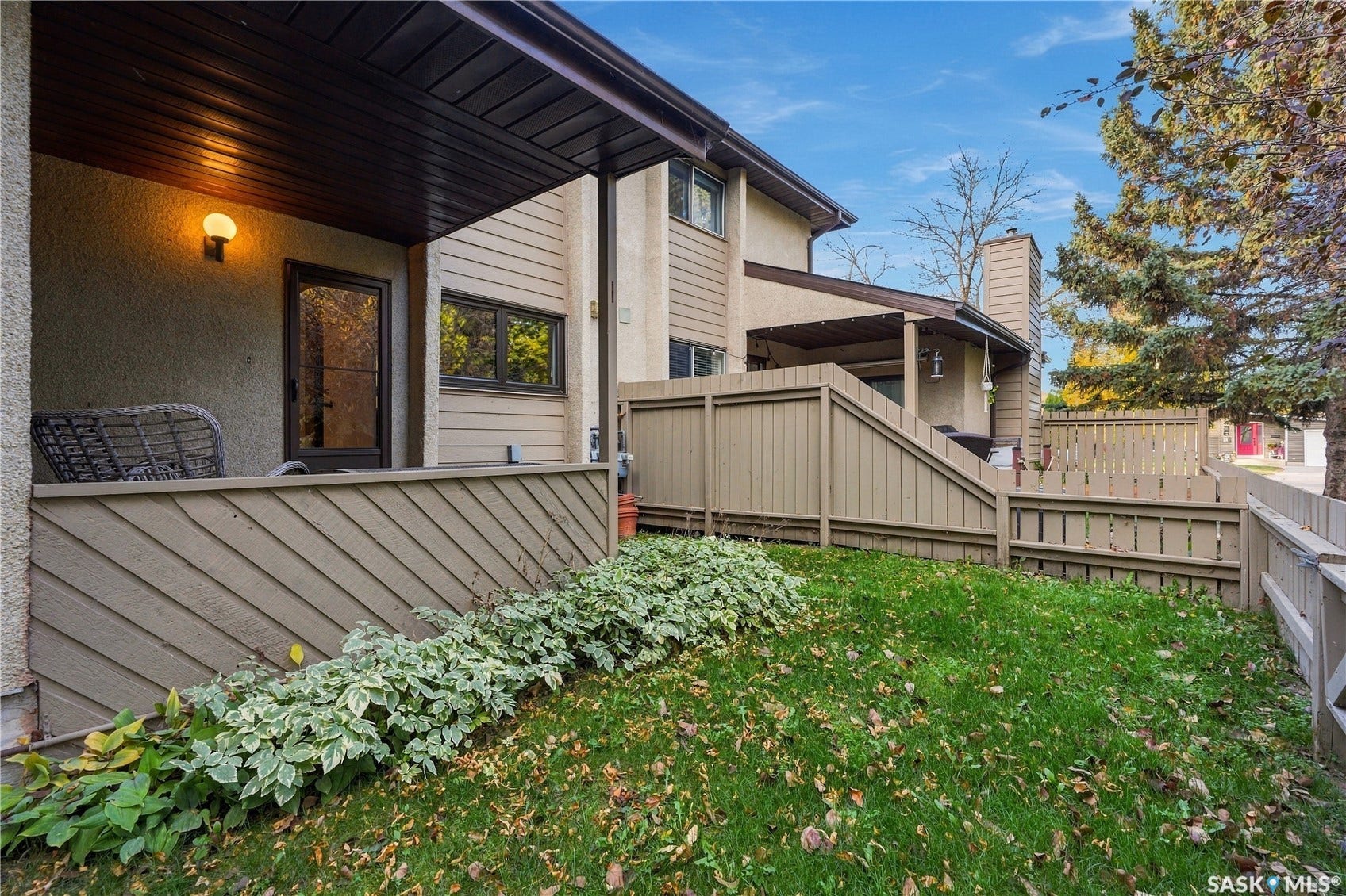 Covered patio entry with exterior lighting, stucco siding, wood plank fencing, and mature landscaping