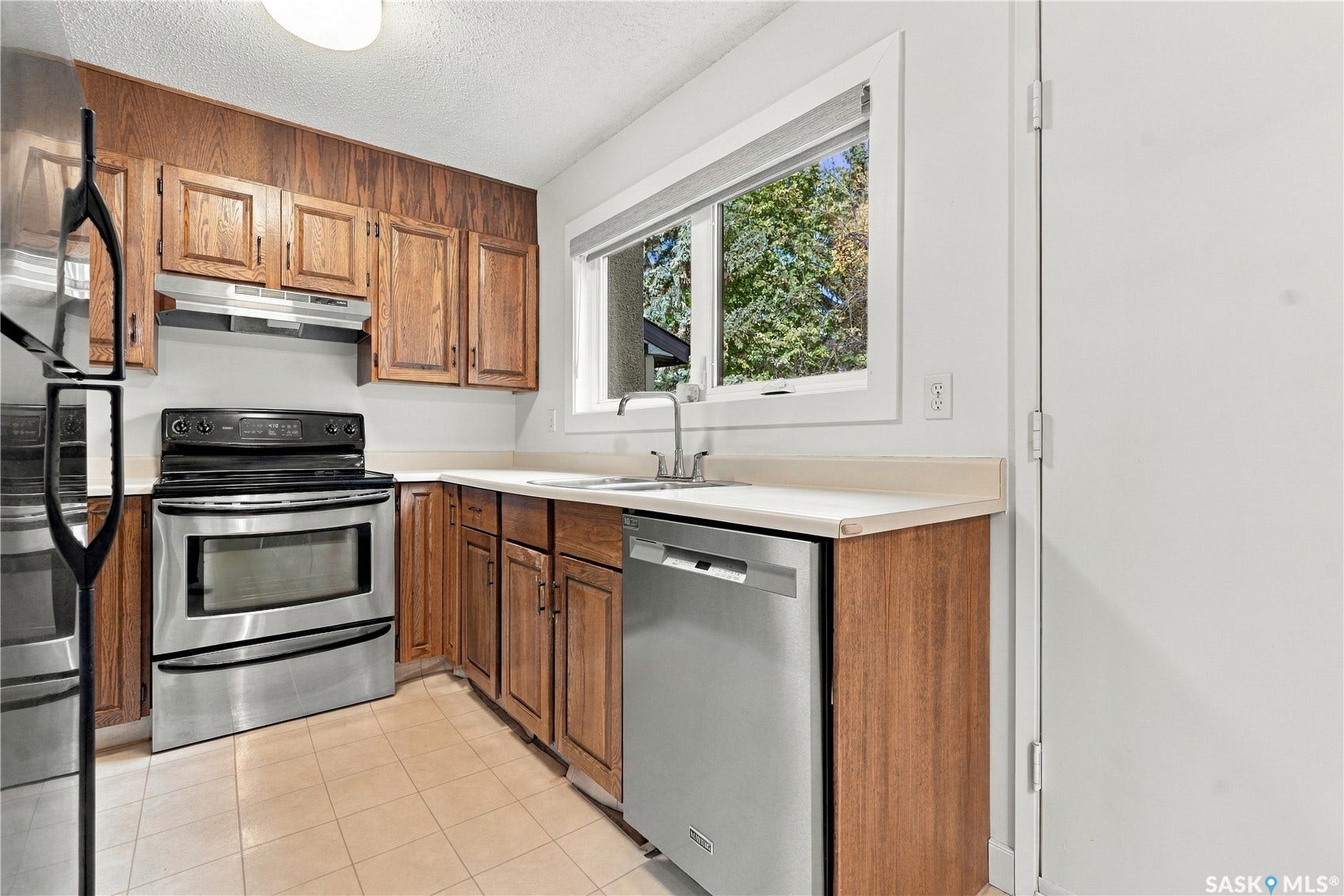 Kitchen featuring stainless steel appliances, wood cabinetry, light-toned countertops, and a window above the sink
