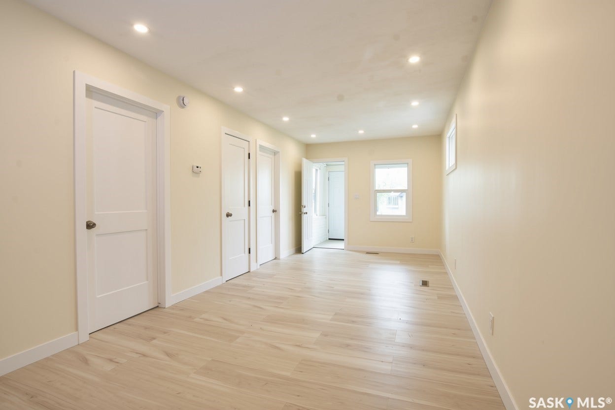 New recessed lighting illumination, light-toned vinyl plank flooring, multiple panel doors with hardware, neutral wall color, and a window with white trim