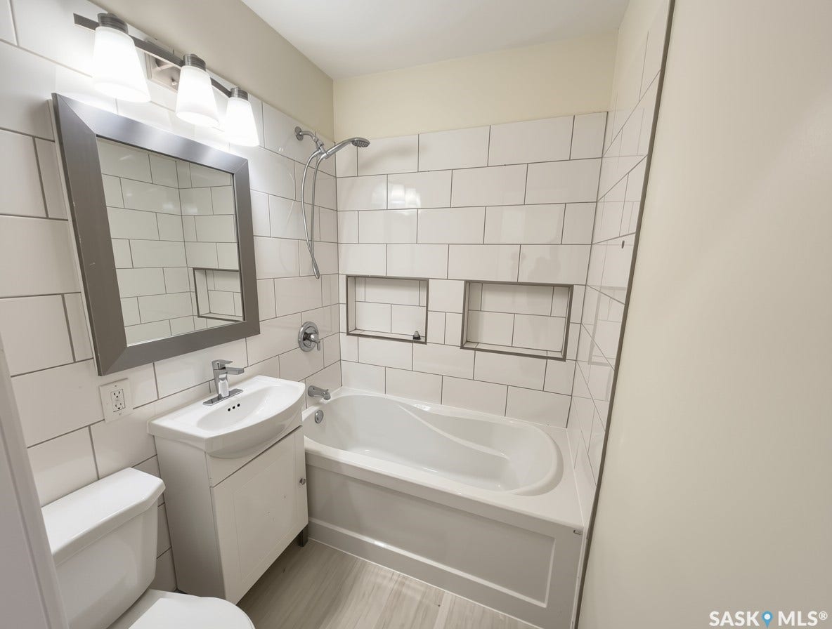 Bathroom featuring subway tile walls, a built-in tub with a shower fixture, a vanity with an integrated sink, a framed mirror, and vinyl plank flooring